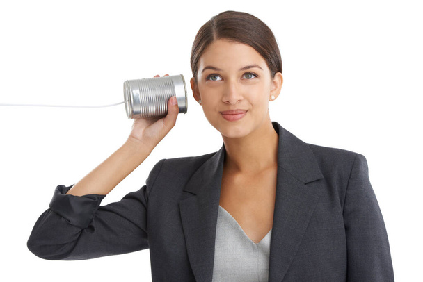 Ouderwetse communicatie. Studio shot van een aantrekkelijke jonge zakenvrouw luisteren naar haar tin kan telefoneren. - Foto, afbeelding