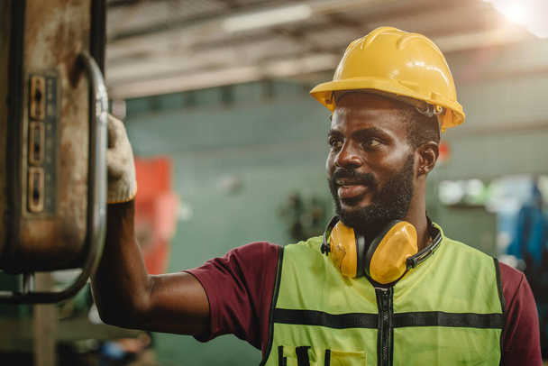 Siyahi Afrikalı profesyonel işçi, ağır sanayi fabrikasında çalışıyor. Güvenlik için mühendis kıyafeti ve kask giyiyor. İşçi çalışma makinesi.. - Fotoğraf, Görsel