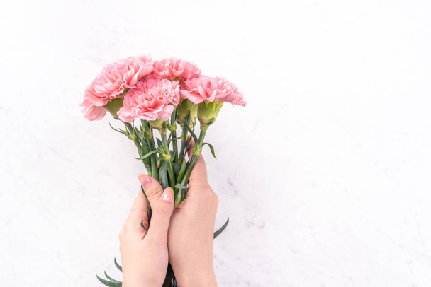Woman giving bunch of elegance blooming baby pink color tender carnations isolated on bright marble background, mothers day decor design concept, top view, close up, copy space - Fotoğraf, Görsel