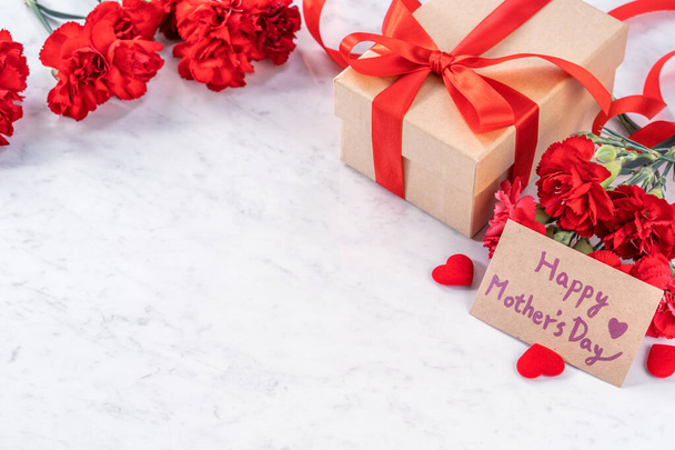 May mothers day handmade giftbox wishes photography - Beautiful blooming carnations with red ribbon bow box isolated on modern marble desk, close up, copy space, mock up - Fotografie, Obrázek
