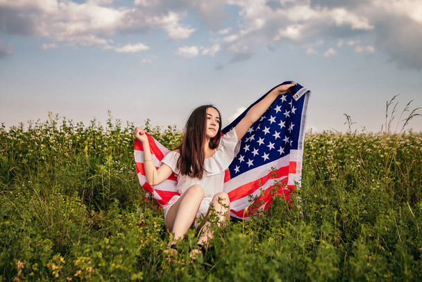 Gelukkige 4 juli! Onafhankelijkheidsdag viert feest. Patriottische vrouw gewikkeld in Amerikaanse vlag zwaaiend op wind en lopend op het veld. Sterren en strepen. Vrijheid. - Foto, afbeelding