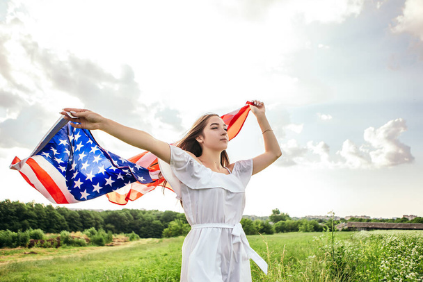 Buon 4 luglio! Festa dell'Indipendenza che celebra. Donna patriottica stretta avvolta nella bandiera nazionale americana che sventola sul vento e cammina sul campo. Stelle e strisce. Concetto di libertà. - Foto, immagini