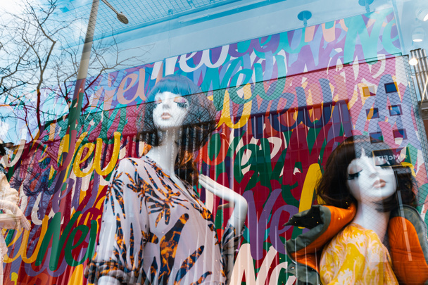 μανεκέν γυναικείων ενδυμάτων σε έντονα χρώματα, πίσω από γυάλινο κατάστημα ρούχων. Γυναικεία μανεκέν με αφηρημένες αντανακλάσεις - Φωτογραφία, εικόνα