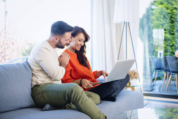 Happy couple relaxing on the couch together. Cheerful woman and handsome man using laptop while browsing on the internet. - Foto, Bild