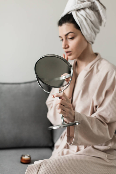 young woman in bathrobe looking at mirror in kitchen - 写真・画像