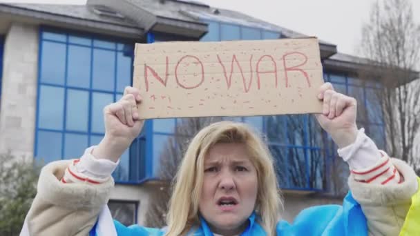 Ukrainan nainen, jolla on vaaleat hiukset ja vakava ele, sininen ja keltainen Ukrainan lippu, jossa lukee: "Ei sotaa", kadulla, huutaen protestoiden Ukrainan ja Venäjän sotaa. - Materiaali, video