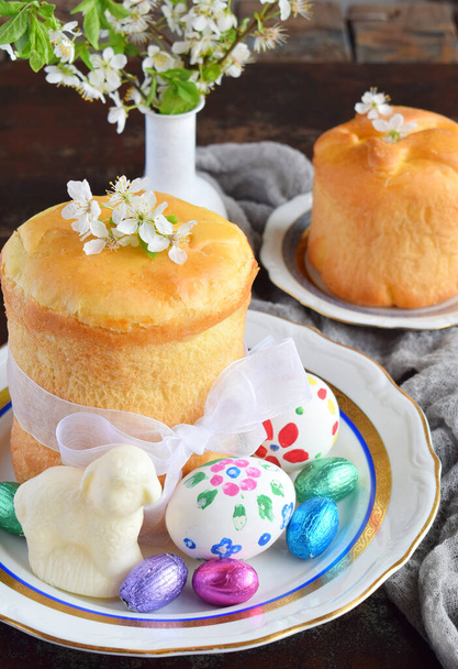Happy Easter concept. Sweet bread with dried fruits and colored eggs. Holidays breakfast. Orthodox kulich. Festive table place setting decoration with paska, blossom twigs, bunny, chocolate egg. - Foto, immagini