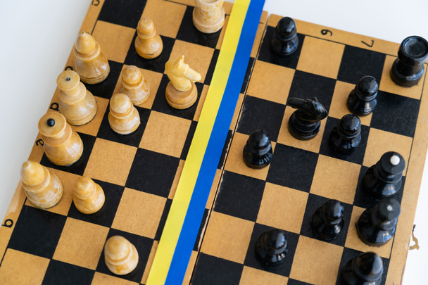 Bovenaanzicht van blauw en geel lint op schaakbord geïsoleerd op wit - Foto, afbeelding