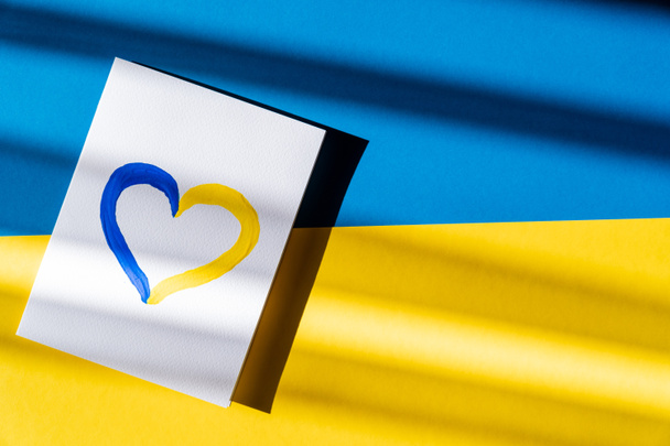Vista dall'alto di dipinto giallo e blu segno del cuore su carta sulla bandiera ucraina - Foto, immagini