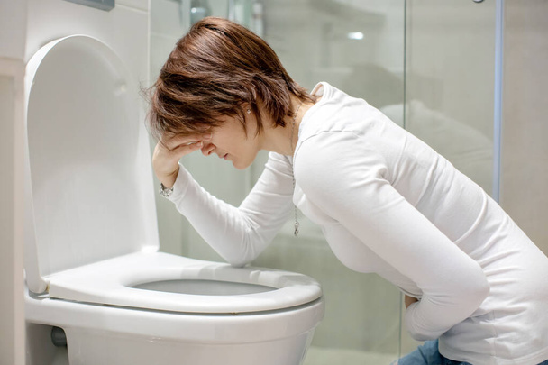 Woman, girl, experiencing sickness, vomiting, pregnancy, poisoning and morning discomfort, sitting over the toilet - Foto, afbeelding