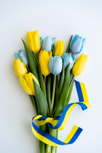 Vista superior del ramo de tulipanes con cinta azul y amarilla sobre fondo blanco  - Foto, imagen
