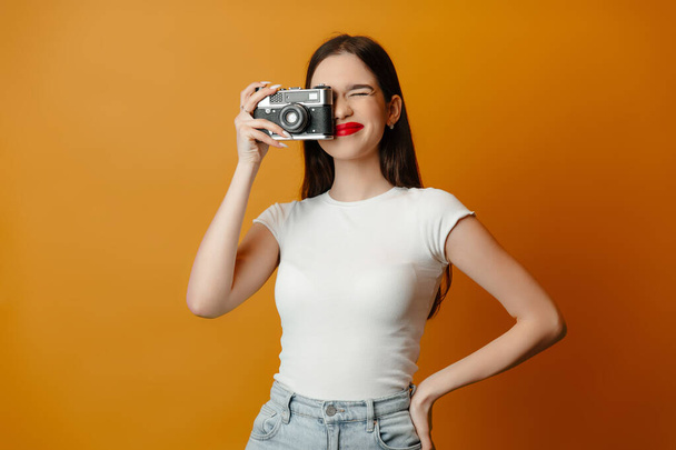 Brunette is standing isolated against the bright background. The girl is holding a camera in the right hand - Fotografie, Obrázek