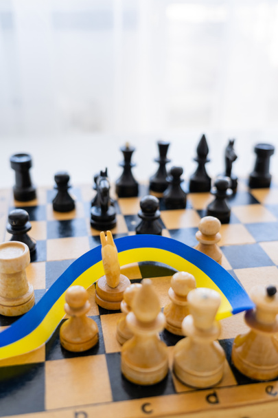 Cinta azul y amarilla sobre tablero de ajedrez borroso sobre fondo blanco  - Foto, imagen