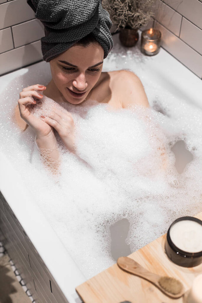 mujer joven relajándose en la bañera con espuma y toalla - Foto, imagen