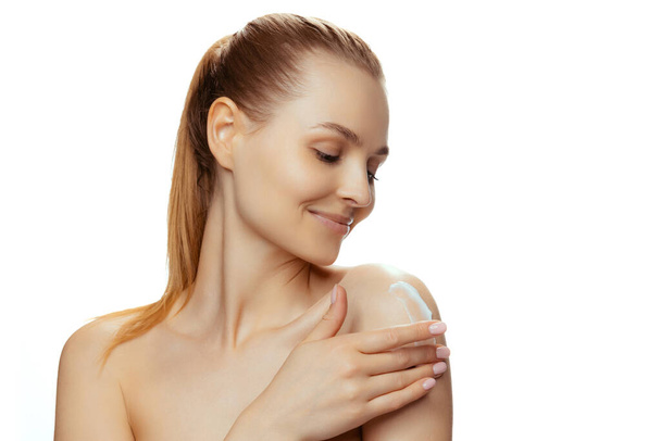 Portrait of young beautiful woman moisturizing skin with cream isolated over white studio background - Φωτογραφία, εικόνα