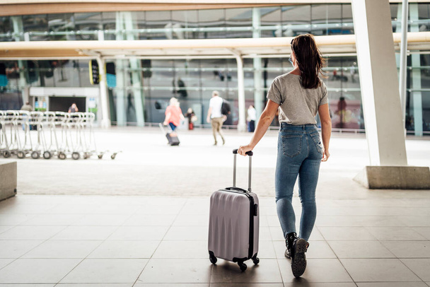 Una joven con máscara caminando con el equipaje al aeropuerto - Foto, imagen