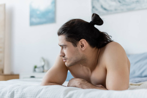 shirtless man looking away while lying on bed at home - Foto, Imagem