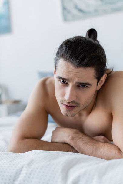 shirtless man looking at camera while lying on bed - Fotoğraf, Görsel