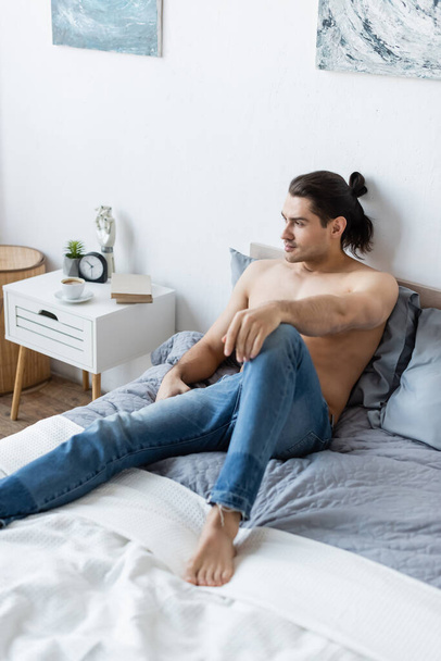verträumter Barfußmann in Jeans, der zu Hause auf dem Bett liegt - Foto, Bild