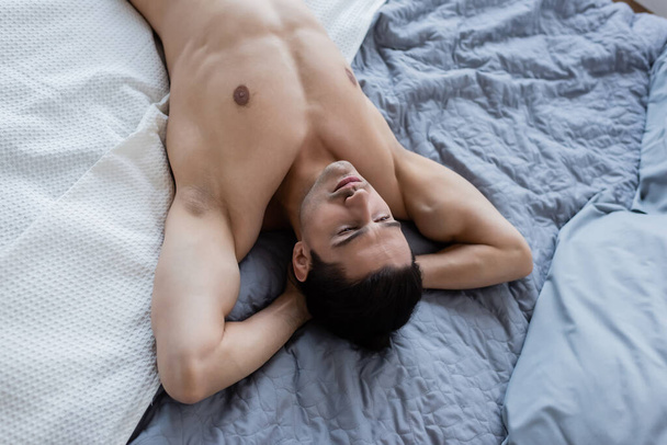 top view of shirtless man lying on bed at home - Fotó, kép