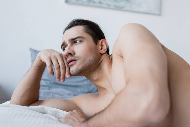 shirtless man resting on bed and looking away - Fotó, kép
