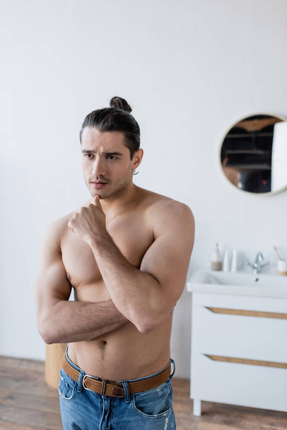 muskularny mężczyzna z długimi włosami patrząc daleko w nowoczesnej łazience  - Zdjęcie, obraz