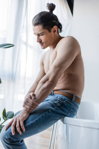 shirtless man with long hair sitting on white bathtub  - Foto, Bild