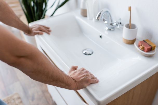 abgeschnittene Ansicht eines Mannes, der sich auf ein weißes Waschbecken im Badezimmer lehnt  - Foto, Bild