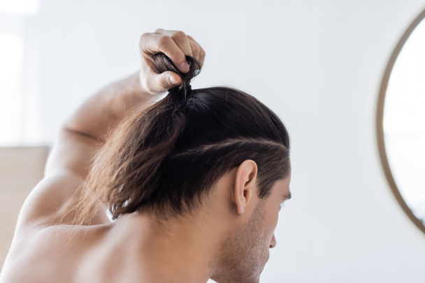 back view of man styling long hair in bun  - Photo, Image