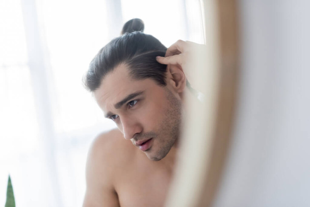 shirtless man with hair bun looking at mirror  - Foto, afbeelding