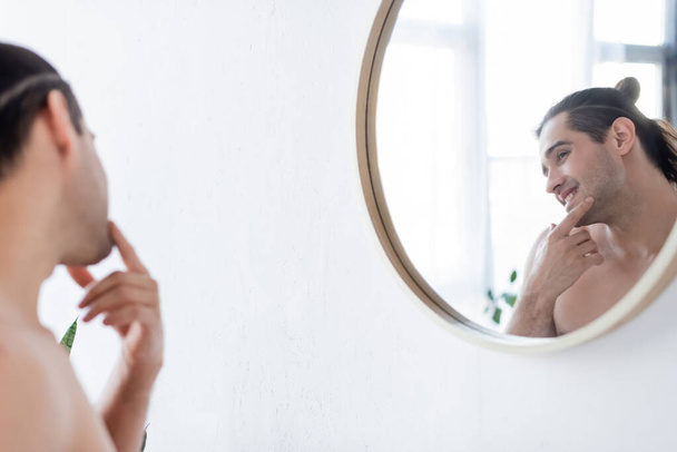 cheerful and shirtless man smiling while looking at mirror in bathroom  - Fotoğraf, Görsel