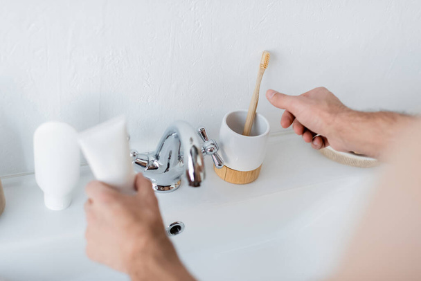 обрезанный вид человека, держащего зубную пасту трубки в ванной комнате - Фото, изображение