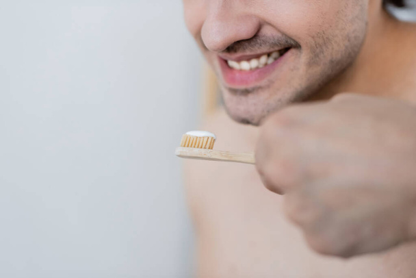 vista ritagliata dell'uomo allegro che tiene lo spazzolino da denti con dentifricio in bagno - Foto, immagini