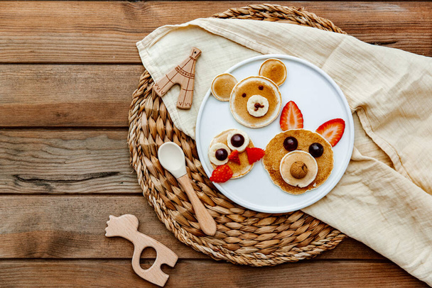 Pancakes With Funny Faces Decorated For Kids. Healthy Fruit Pancakes For baby Meal over wooden background, top view - Foto, immagini