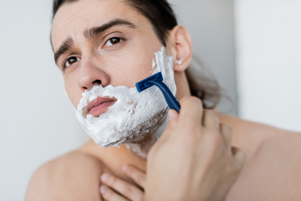 félmeztelen férfi habbal az arcán borotválkozás a fürdőszobában  - Fotó, kép