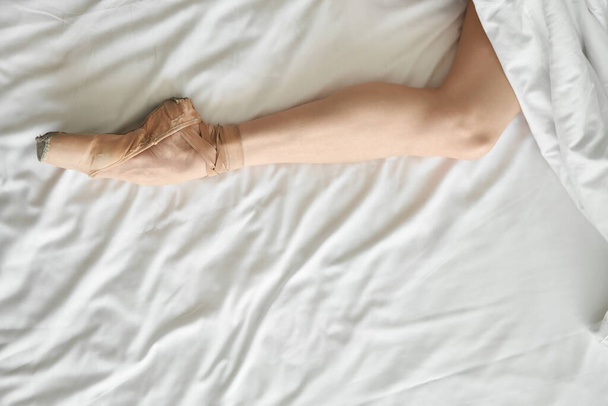 Woman in pointe shoe shows her leg from under coverlet - Foto, immagini