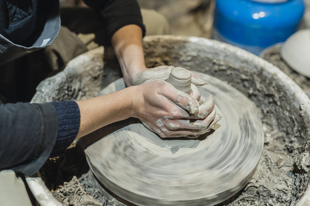 potter's female hands, soiled in clay, form clay lump on potter's wheel. Craft clay pottery, hobby folk art. Potter's hands close-up, on potter's wheel, in clay, making ceramics - 写真・画像