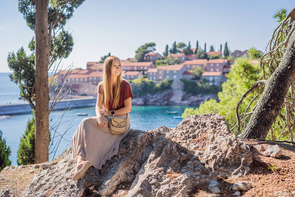 Woman tourist on background of beautiful view of the island of St. Stephen, Sveti Stefan on the Budva Riviera, Budva, Montenegro. Travel to Montenegro concept - 写真・画像