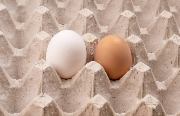 Huevos orgánicos crudos blancos y marrones con enfoque selectivo en bandeja de cartón. Ingrediente para un desayuno saludable con proteínas. Dieta Keto. Dos huevos de ave para plato tradicional de Pascua - Foto, imagen