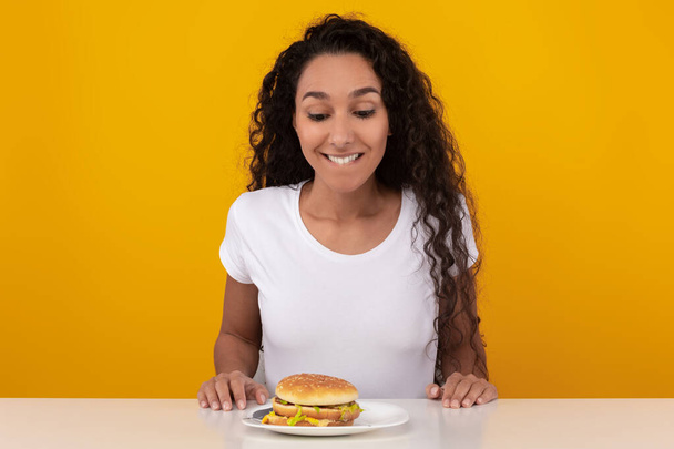 Смешная латиноамериканка смотрит на бургер в студии - Фото, изображение