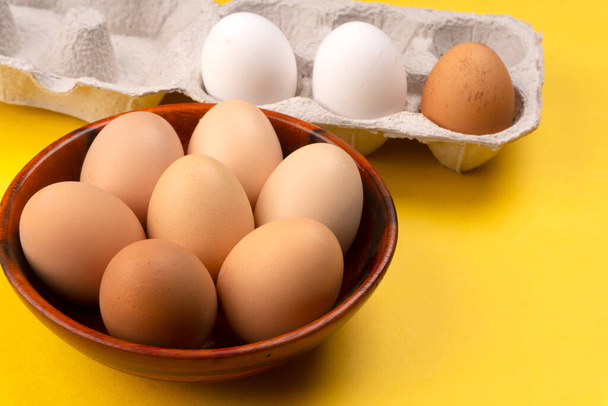 Raw eggs in bowl and box on yellow background - Photo, Image