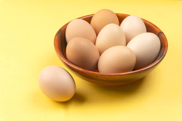 Ξύλινο μπολ με αυγά κοτόπουλου σε κίτρινο φόντο, κοντινό πλάνο  - Φωτογραφία, εικόνα