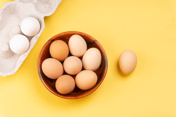 Wooden bowl of chicken eggs on yellow background, closeup shot  - Foto, Bild