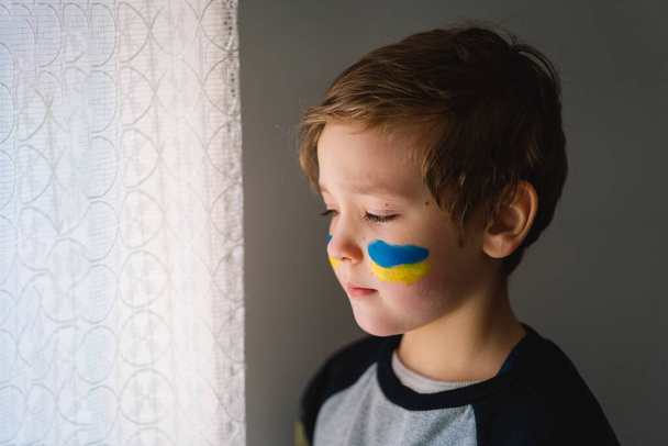 Porträt eines ukrainischen Jungen mit einem Gesicht, das mit den Farben der ukrainischen Flagge bemalt ist. - Foto, Bild