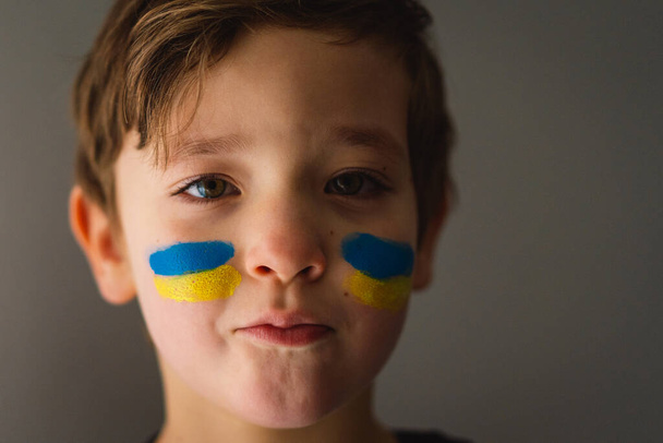 Porträt eines ukrainischen Jungen mit einem Gesicht, das mit den Farben der ukrainischen Flagge bemalt ist. - Foto, Bild