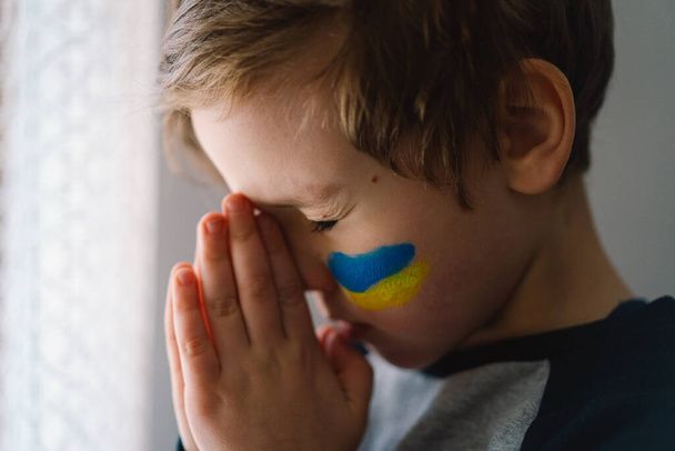 Chico ucraniano cerró los ojos y rezó para detener la guerra en Ucrania. - Foto, imagen