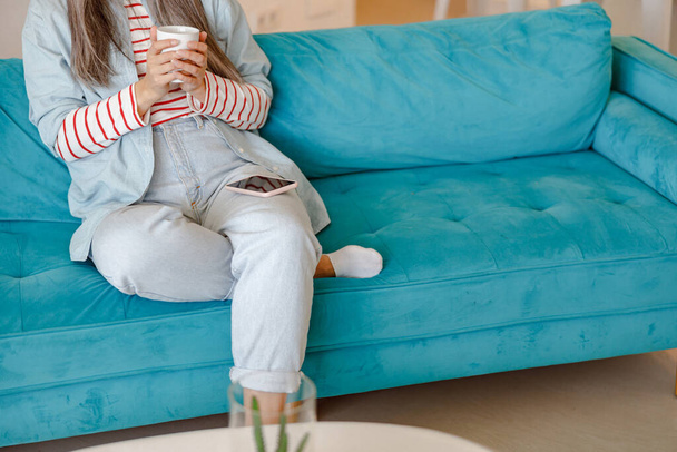 Frau mit Tasse Kaffee und Handy sitzt auf Sofa - Foto, Bild