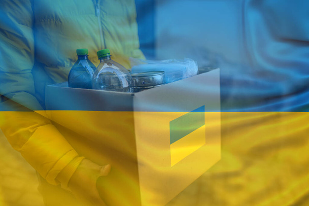 Double exposure of volunteer cyrrying box with Humanitarian aid for Ukrainian refugees and Ukrainian flag. - Foto, Bild