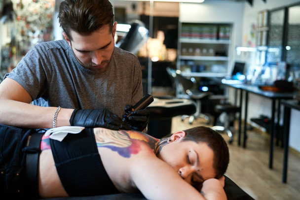 Сосредоточьтесь на кавказском мужчине, татуирующем спину ее клиента - Фото, изображение