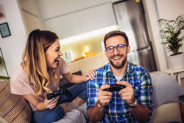 Young couple sitting on a couch in a living room and playing video games - Foto, afbeelding